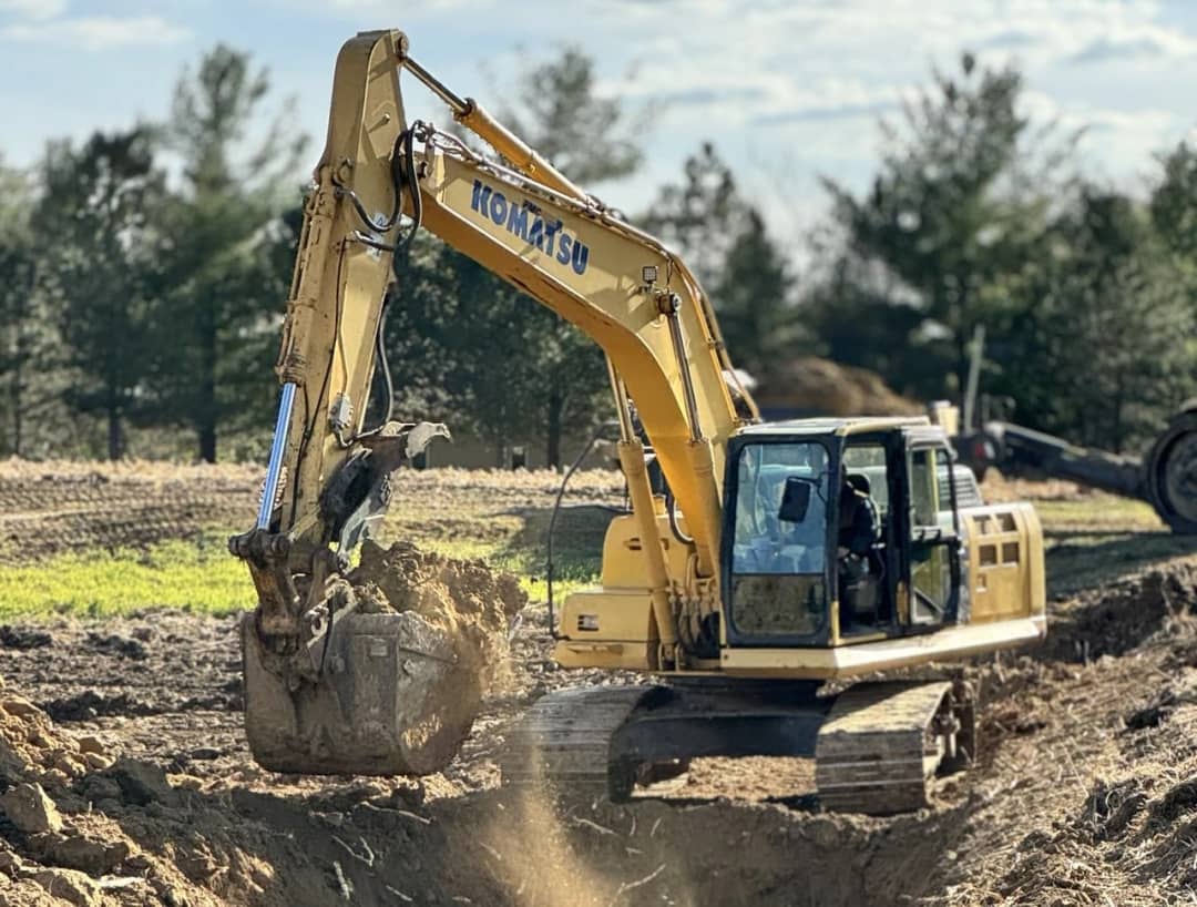 Bright yellow agricultural tractor with digging attachment plowing brown soil on a sunny day