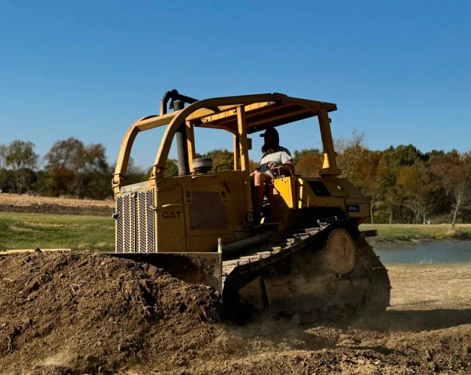 Bright yellow agricultural tractor with digging attachment plowing brown soil on a sunny day