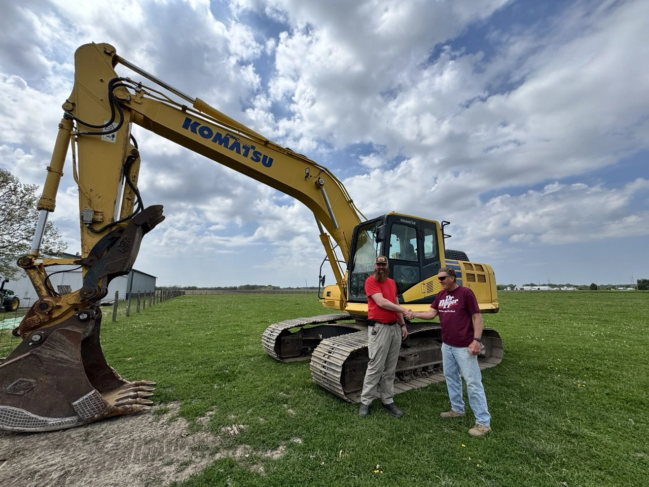 Bright yellow agricultural tractor with digging attachment plowing brown soil on a sunny day